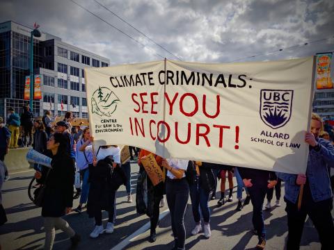 People march along street, hold up sign reading "Climate criminals: see you in court!"