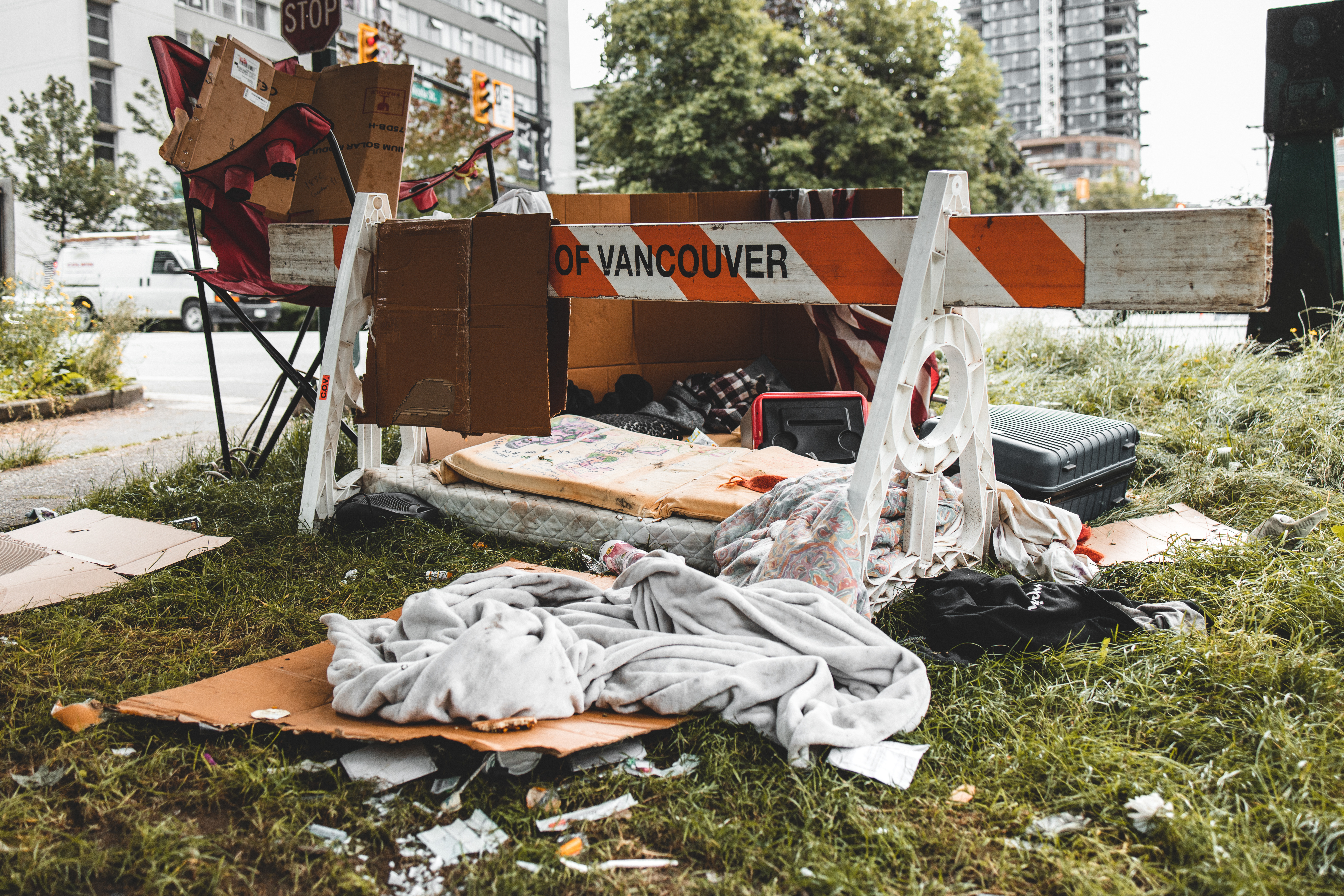 Photo showing City of Vancouver traffic barricade surrounded by blanket, mattress, chair and other belongings and waste