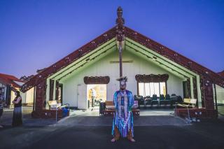 Peyal Francis Laceese, A Tsilhqot’in culture keeper, stands in front of a Marae (Māori spiritual house) in traditional Tsilhqot’in regalia. It is a symbol of the connection and bond between these two Indigenous communities. Photo: Keith Koepke, Kanative Photography.