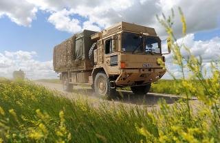 Canadian military lorry traversing plain road  under bright blue skies and cotton clouds, and surrounded by green and yellow foliage